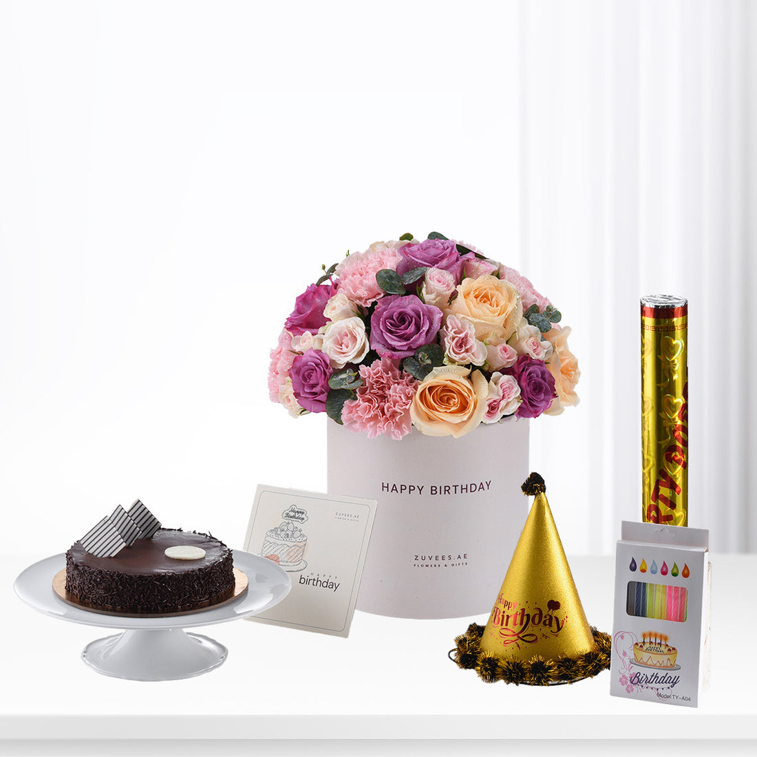 Pink, purple, and peach roses in white box with cake, hat, and candles.