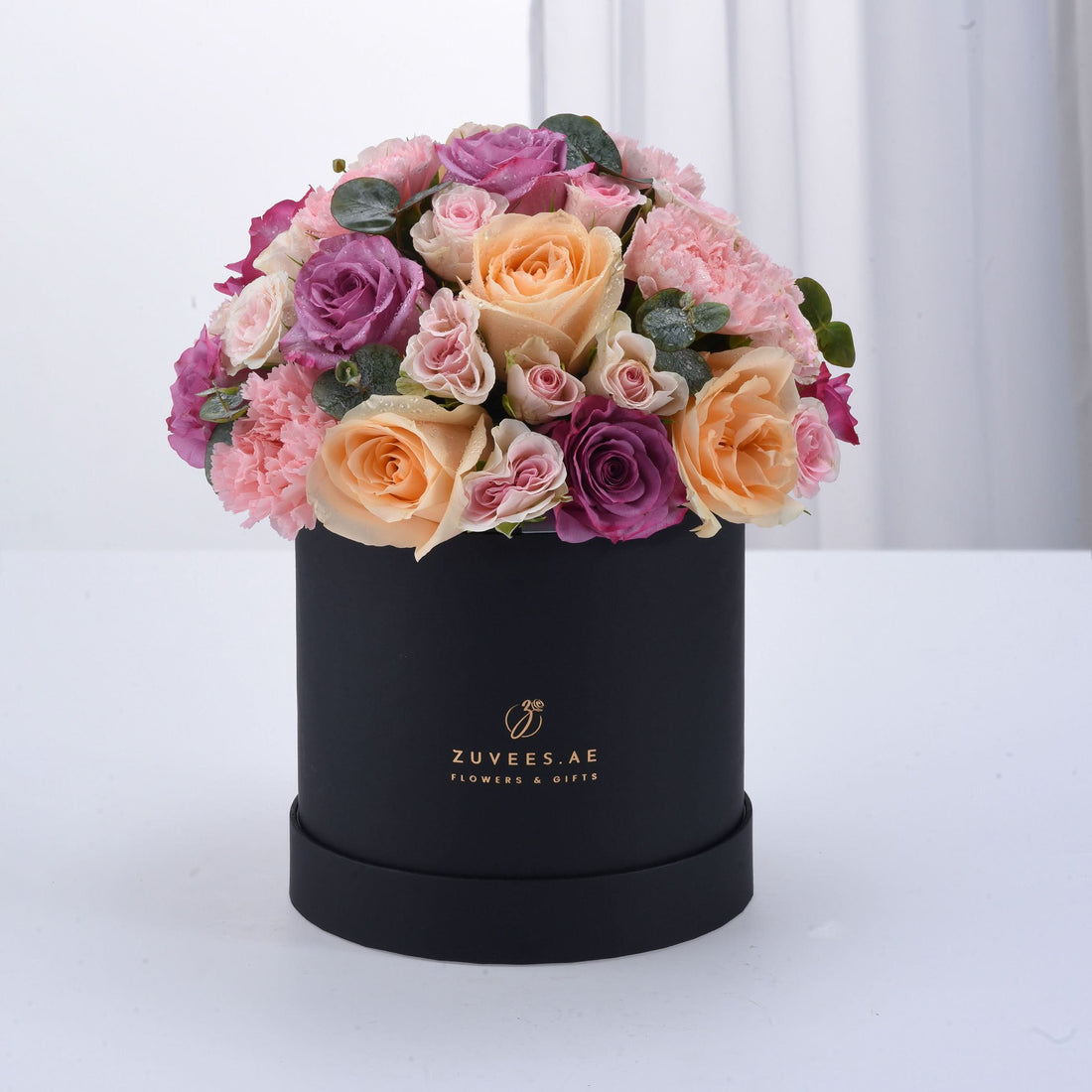 Elegant black box filled with lush pink, peach, and purple roses and carnations.