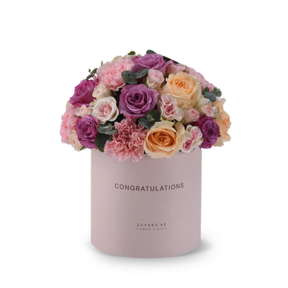 Pink box holds vibrant purple, peach, and pink roses with greenery, "Congratulations" printed.