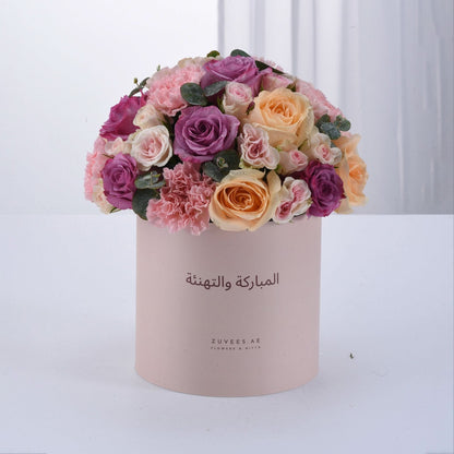 Pastel pink box overflowing with vibrant roses and carnations, Arabic greeting.