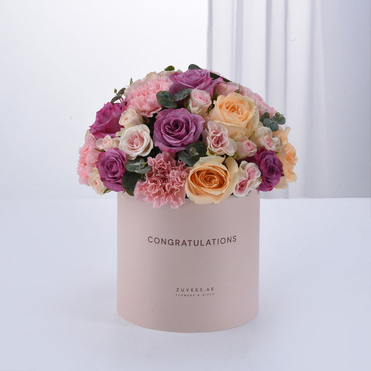 Pastel pink box overflowing with purple, peach, and blush roses and carnations, "Congratulations" printed.
