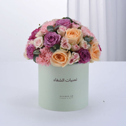 Pastel-hued roses and carnations in mint box with Arabic branding.