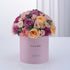 Soft pink box holds lush purple, peach, and blush roses with greenery, celebrating "It&