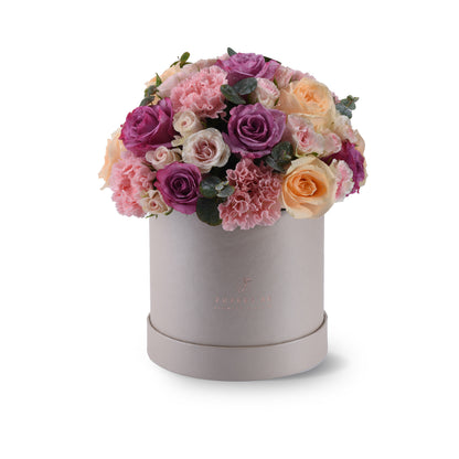 Elegant pastel roses and carnations in a matte silver hatbox.