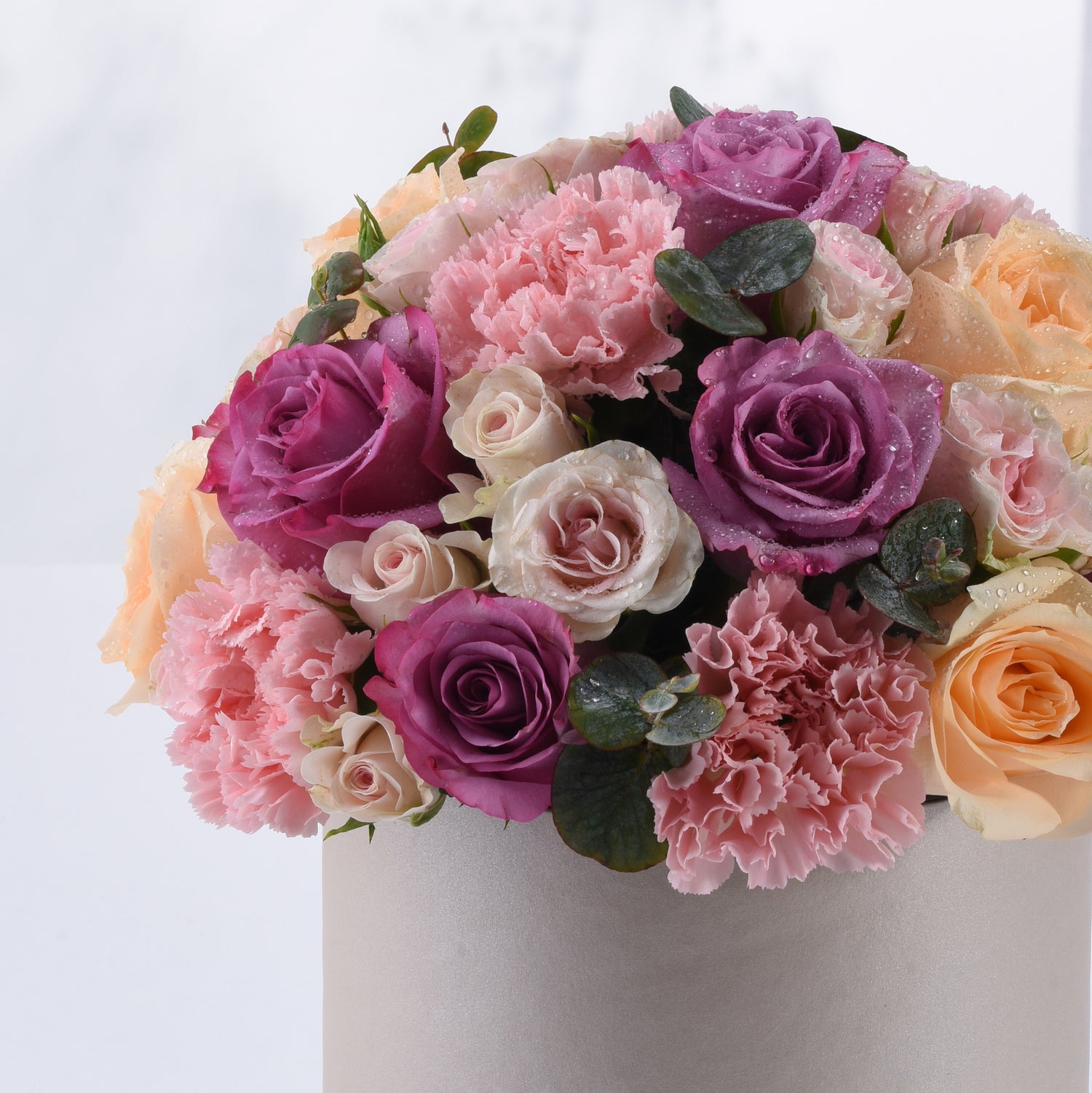 Soft pink, purple, and peach roses with carnations and dewdrops in a silver vase.