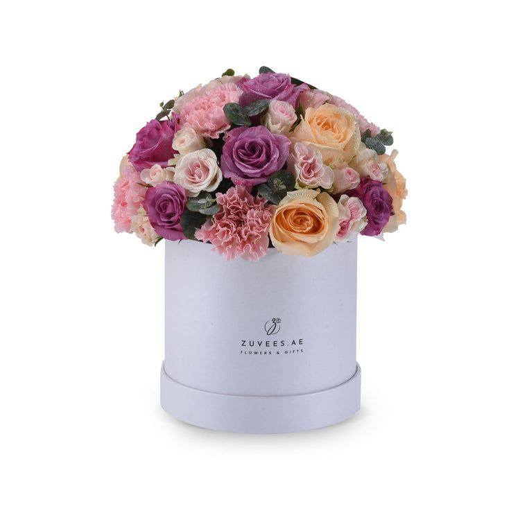 Elegant pastel pink, purple, and peach roses nestled in a sleek white cylindrical box.