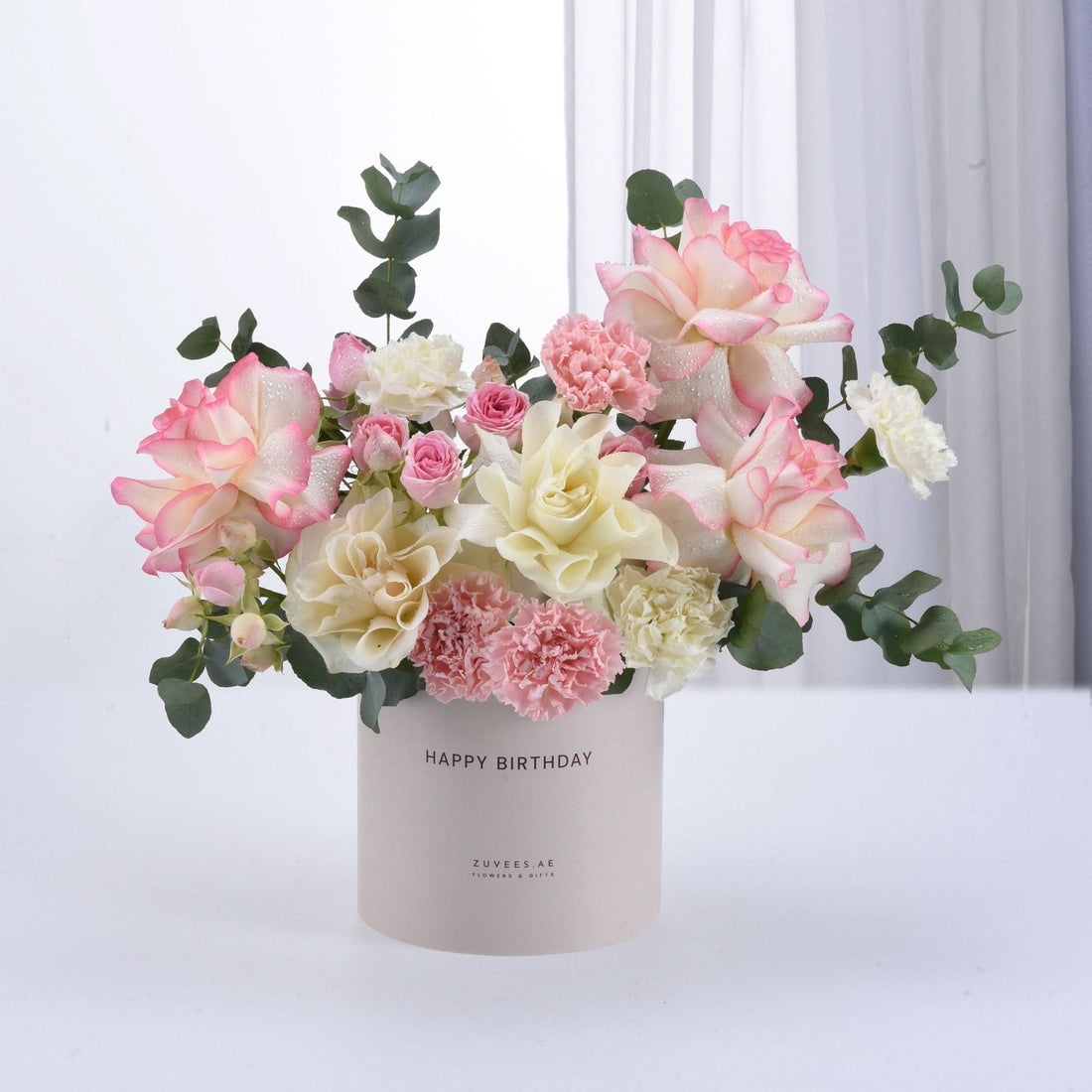 Pastel pink and cream roses with eucalyptus in a "Happy Birthday" cylinder.