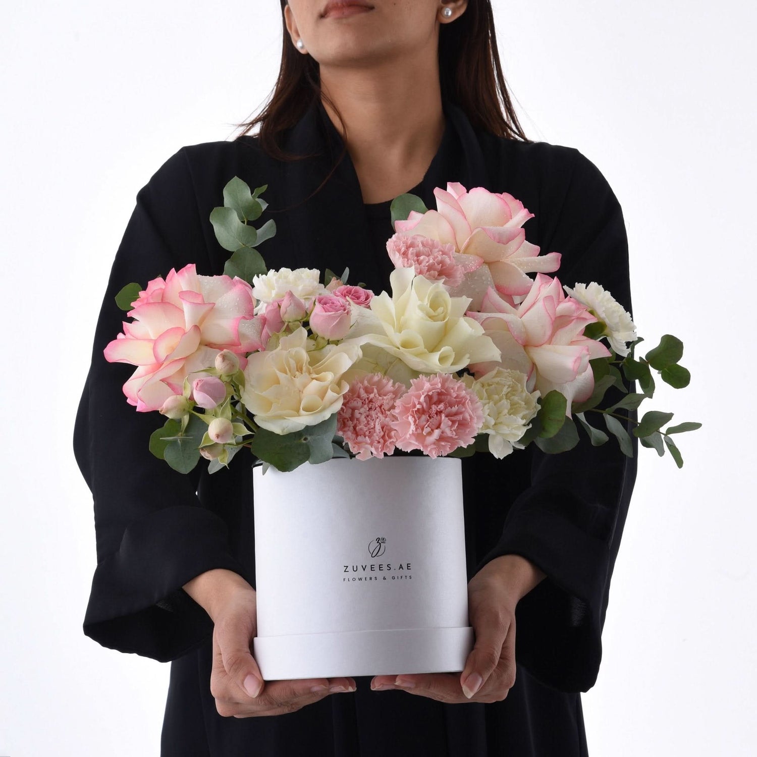 Elegant pink and cream roses with carnations in a white Zuvees gift box, held by woman.