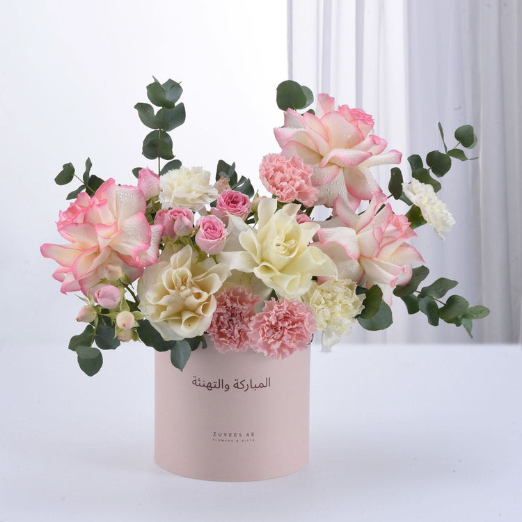 Pastel pink and cream roses, carnations, and eucalyptus in a blush box with Arabic "Congratulations" text.
