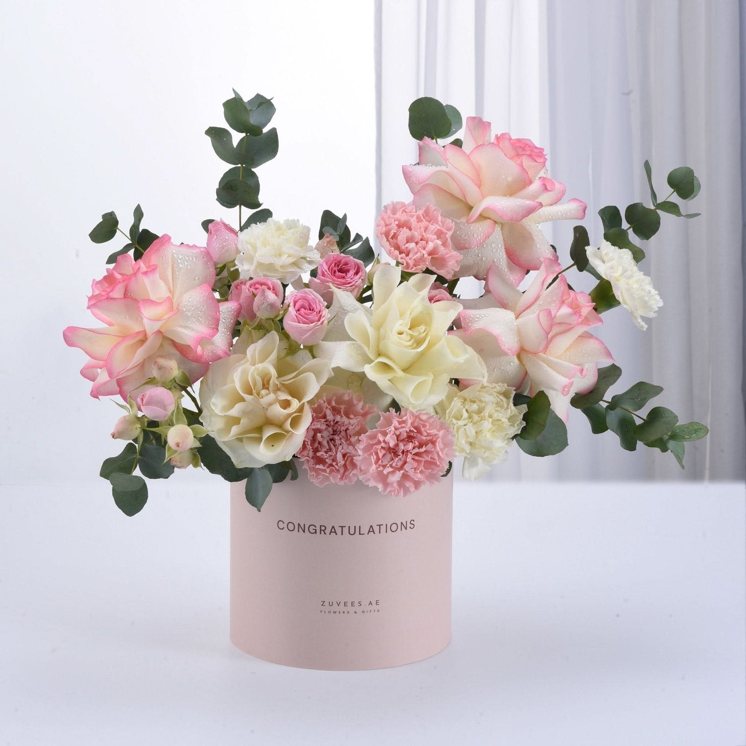 Pastel pink and cream roses, carnations, and eucalyptus in a "Congratulations" box.