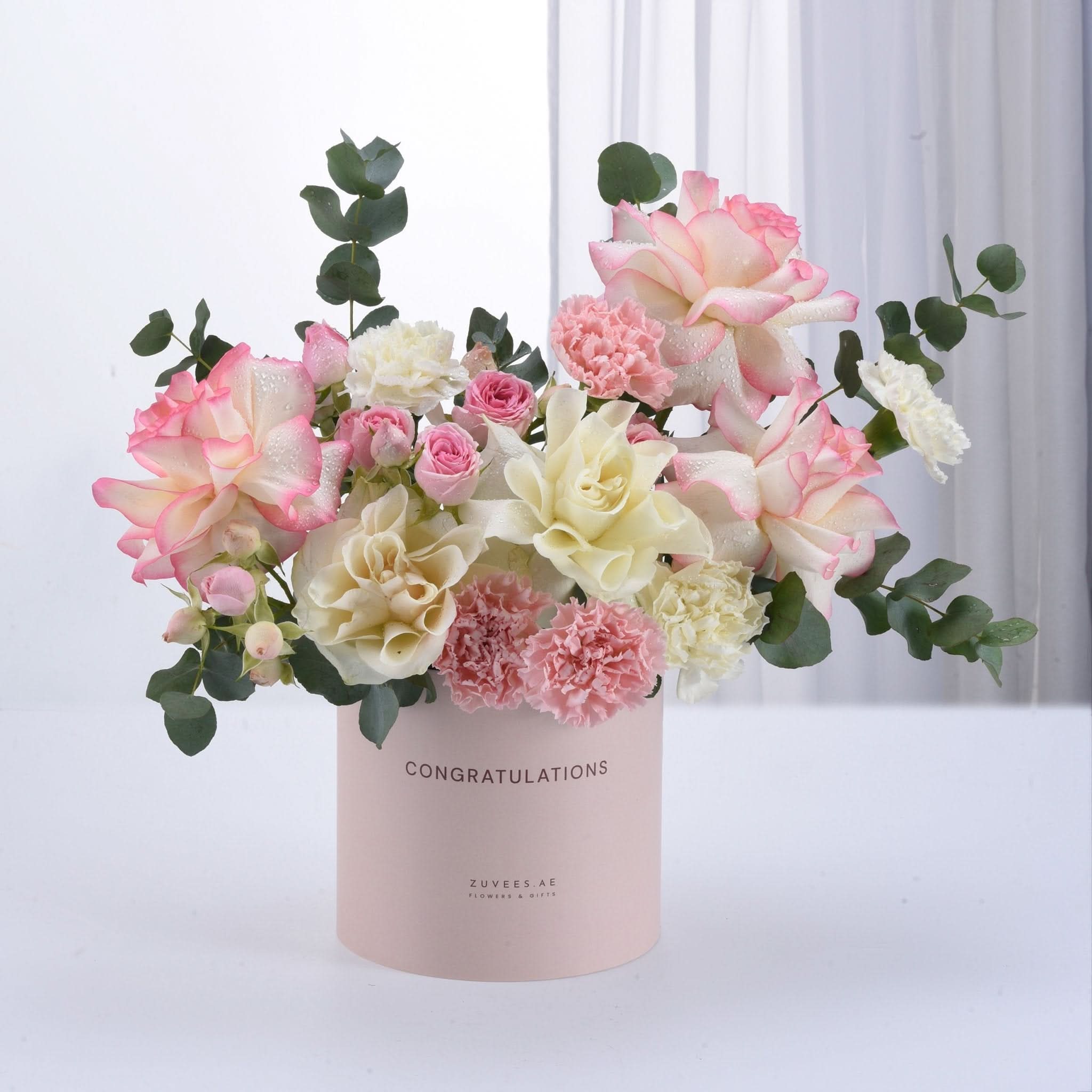 Pastel pink and cream roses, carnations, and eucalyptus in a "Congratulations" box.