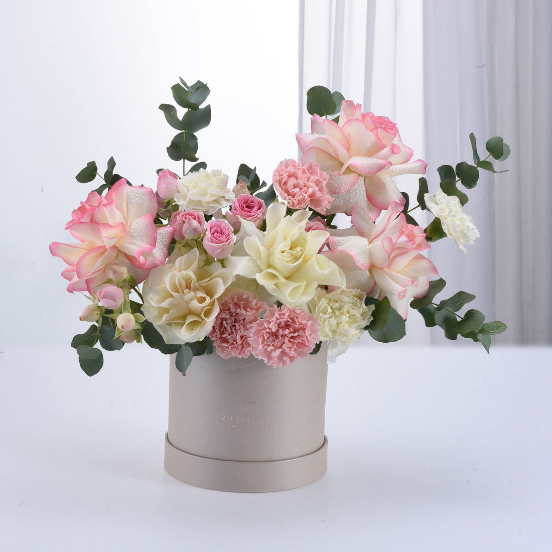 Soft pink and cream roses with carnations in elegant beige box.