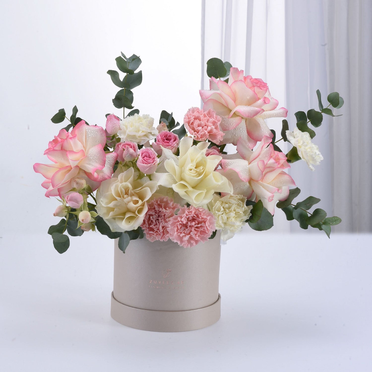Soft pink and cream roses with carnations in elegant beige box.