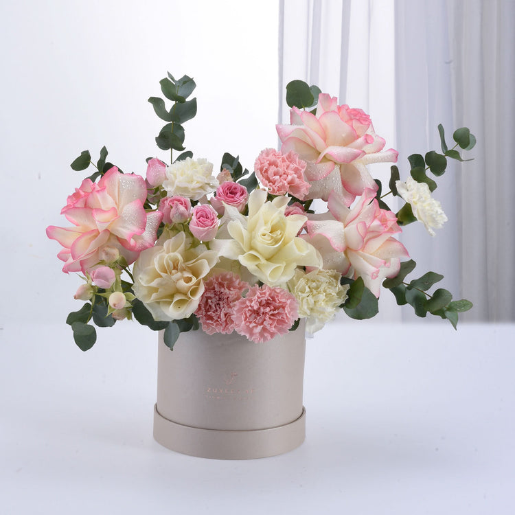 Soft pink and cream roses with carnations in elegant beige box.