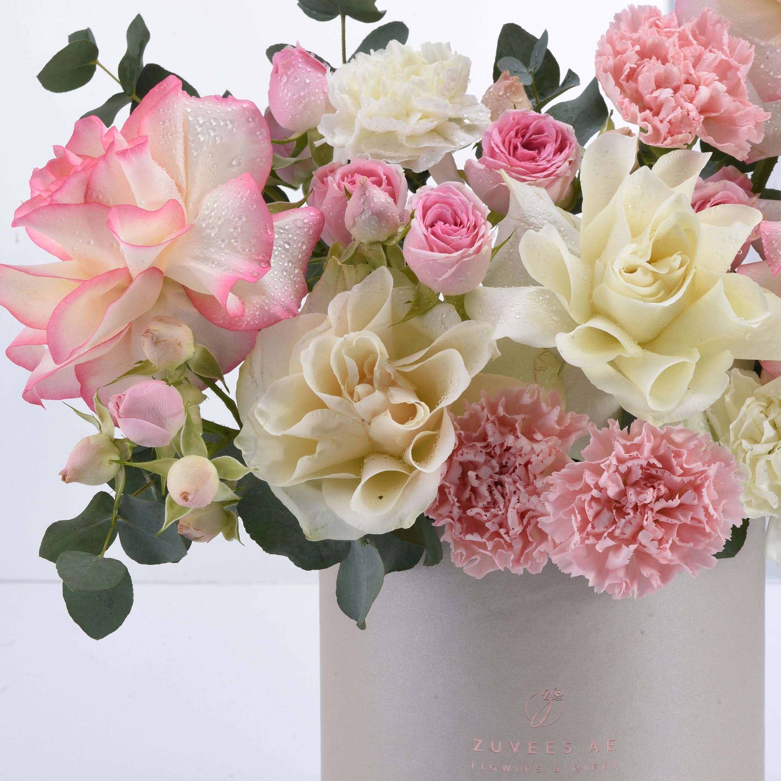Soft pink and cream roses, carnations, dewdrops, eucalyptus in matte pink vase.