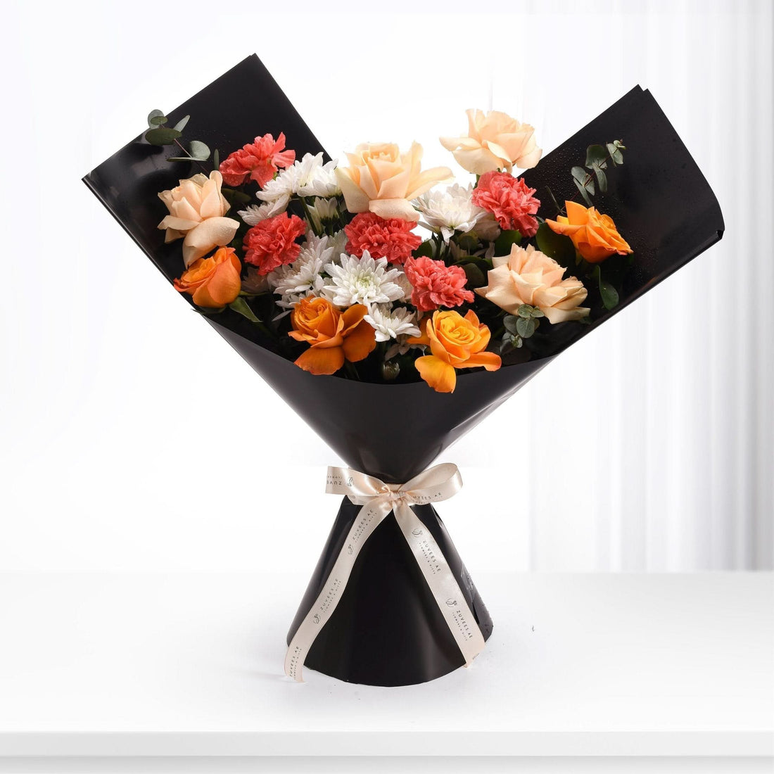 Vibrant orange, peach, red, and white blooms elegantly wrapped in black paper with gold ribbon.