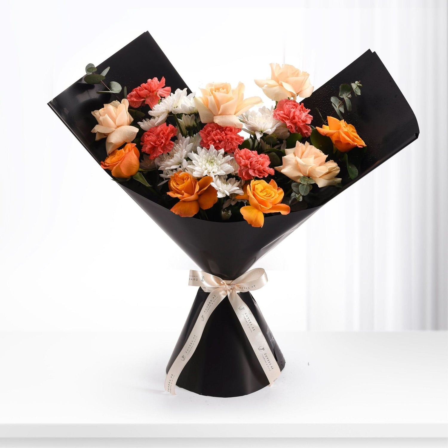 Vibrant orange, peach, red, and white blooms elegantly wrapped in black paper with gold ribbon.