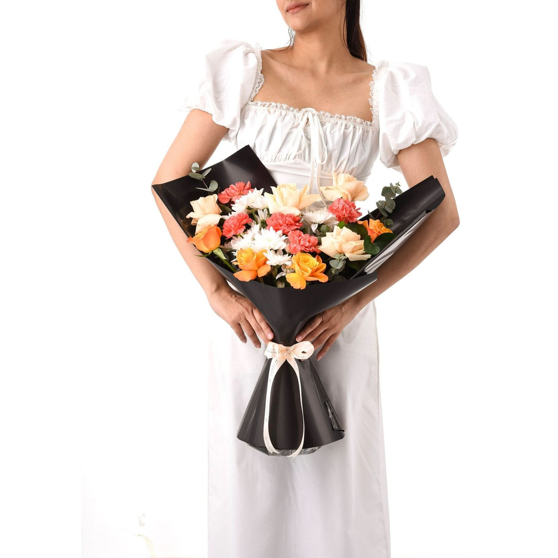 Elegant black-wrapped bouquet with orange, peach, and white blooms, held by a woman in a white dress.