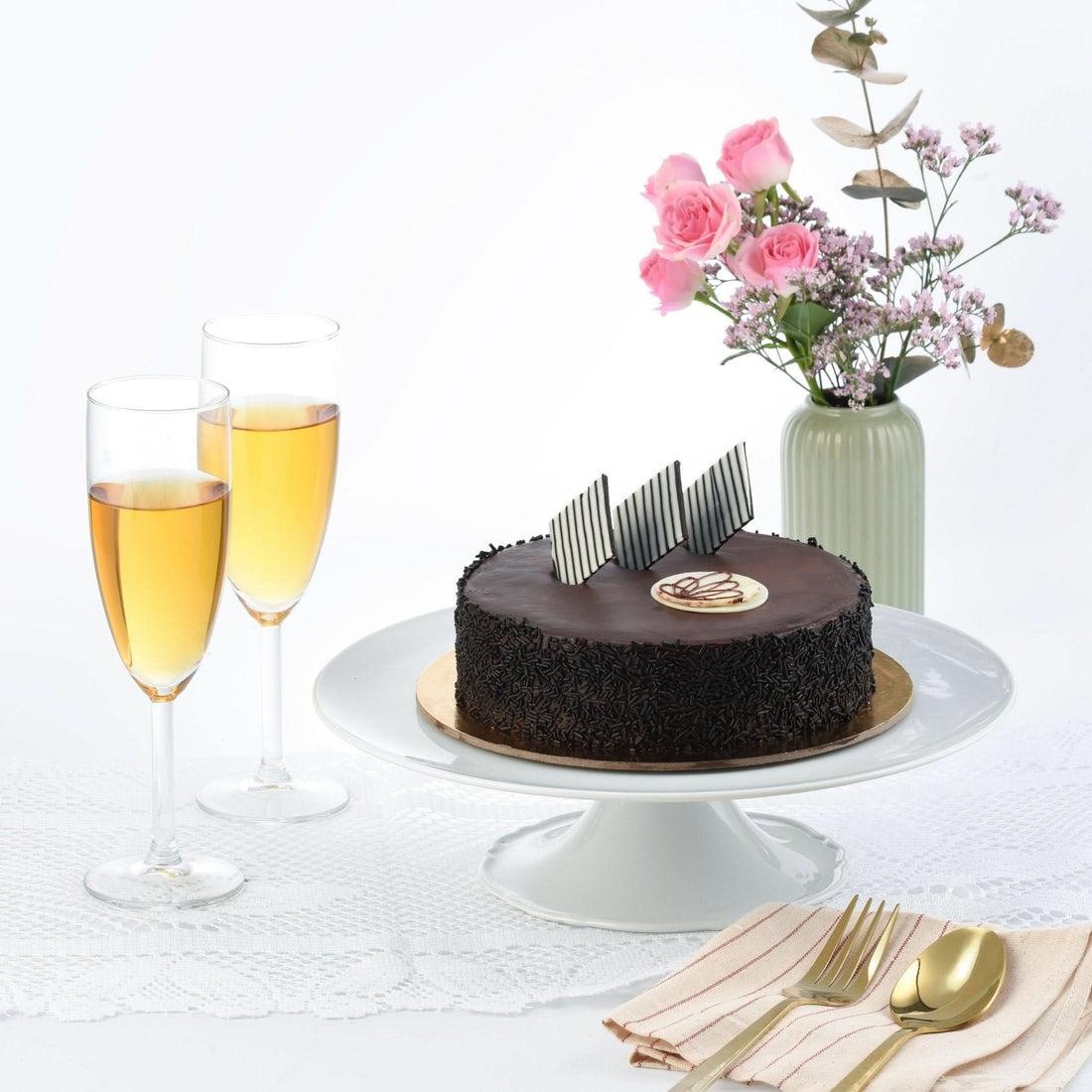 Rich chocolate cake with striped chocolate garnish, champagne flutes, and pink floral arrangement.