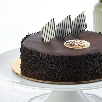 Rich chocolate cake adorned with striped chocolate shards and piped white chocolate design.