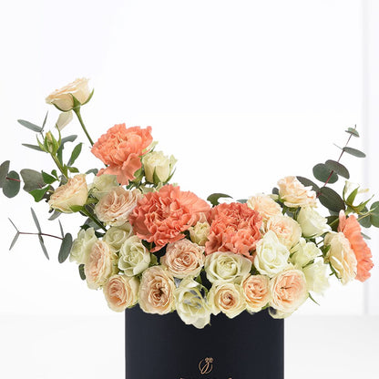 Pastel peach roses and carnations in sleek black vase with eucalyptus.