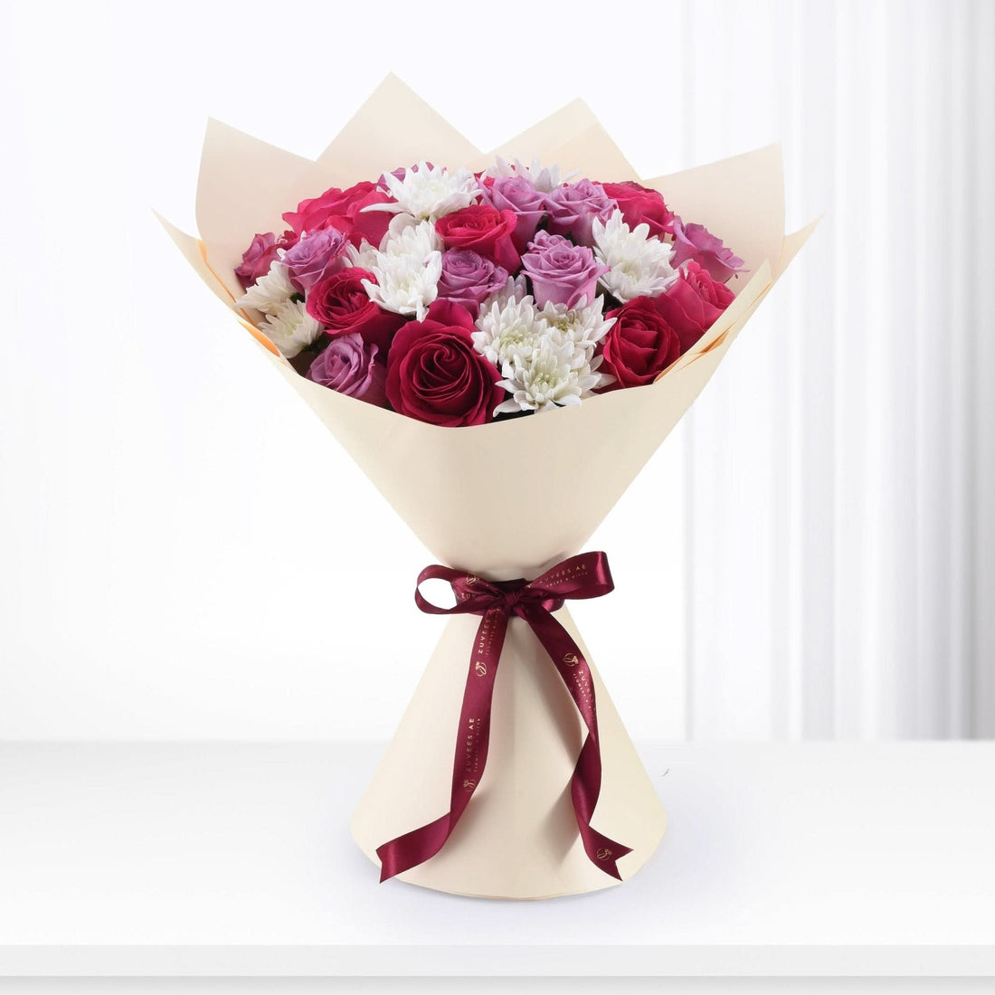 Vibrant red, pink, and white roses with chrysanthemums, elegantly wrapped in cream paper and tied with burgundy ribbon.