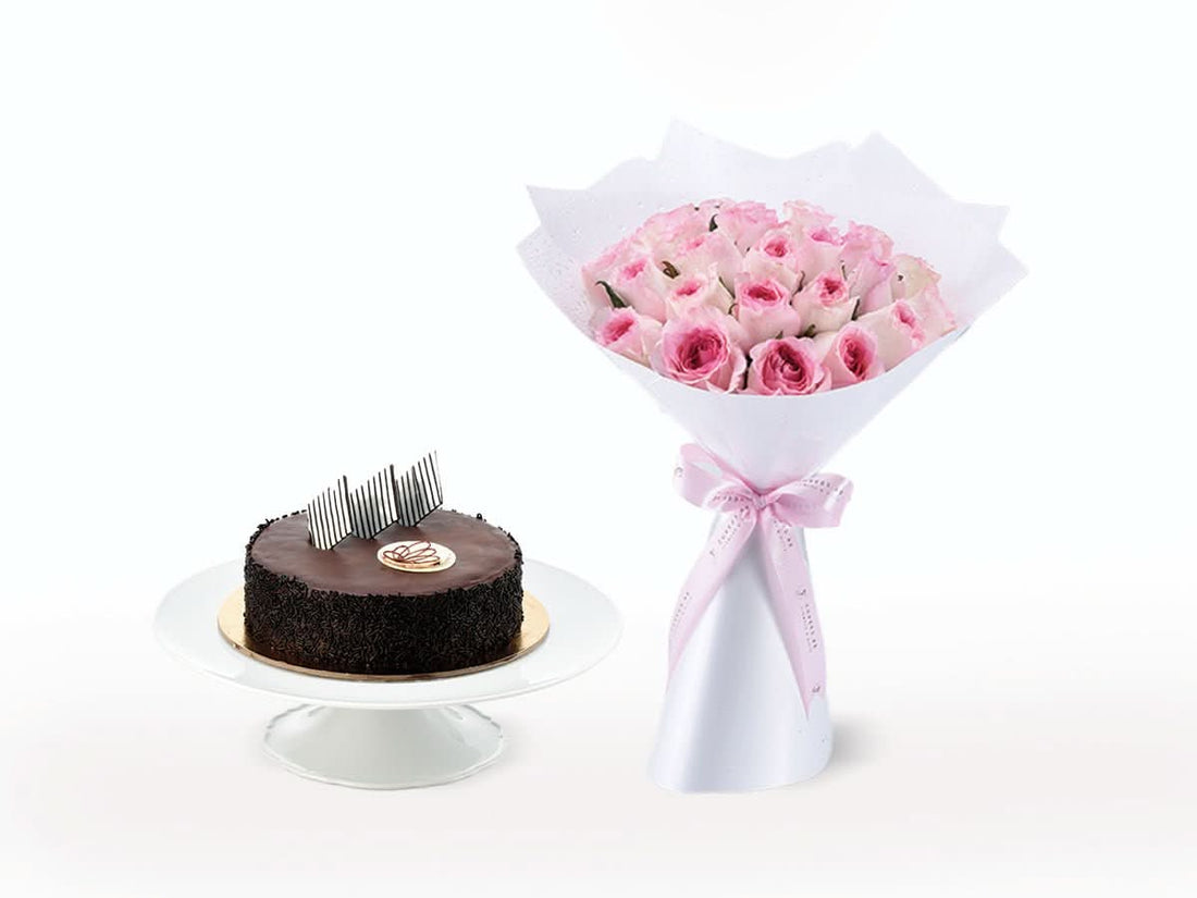 Rich chocolate cake beside elegant pink rose bouquet in white wrap.