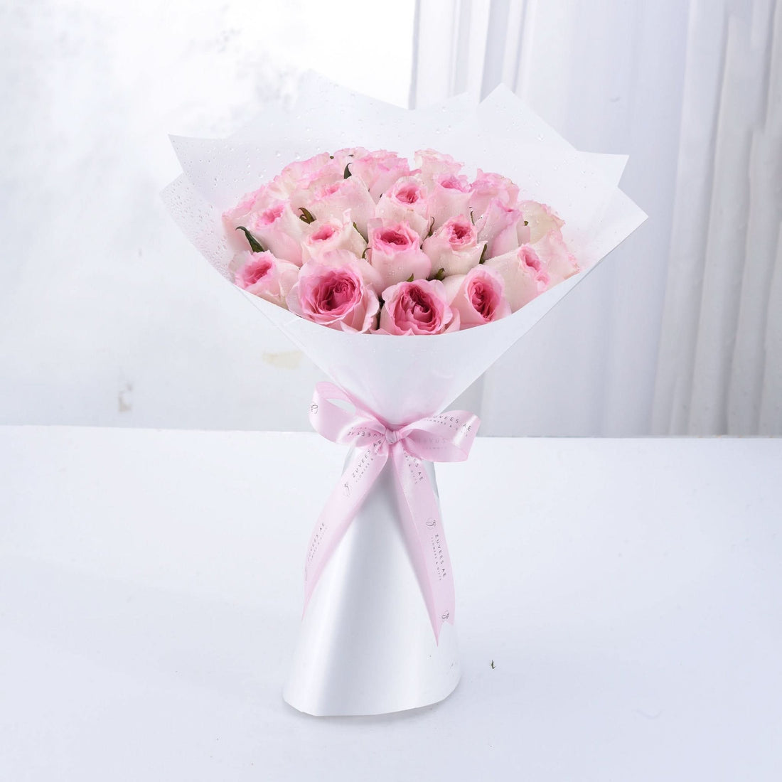 Soft pink roses in white paper, tied with pink ribbon bow.