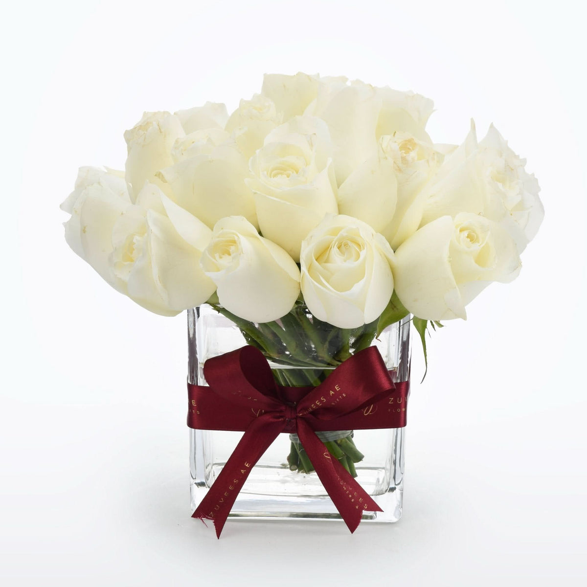 Elegant white roses in clear glass vase, accented with burgundy ribbon.