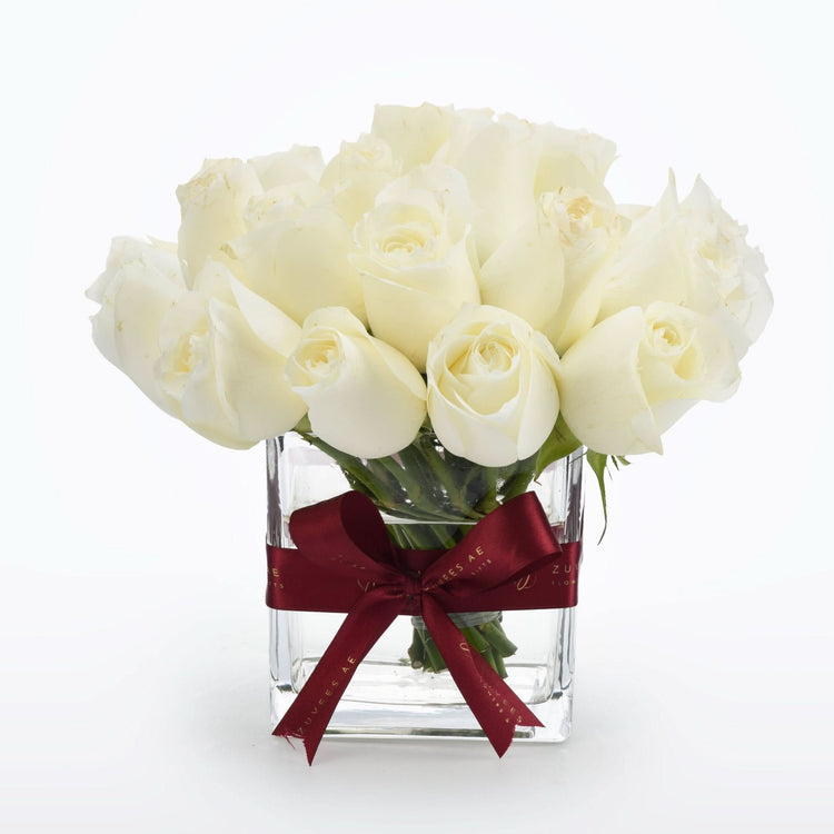Elegant white roses in clear glass vase, accented with burgundy ribbon.