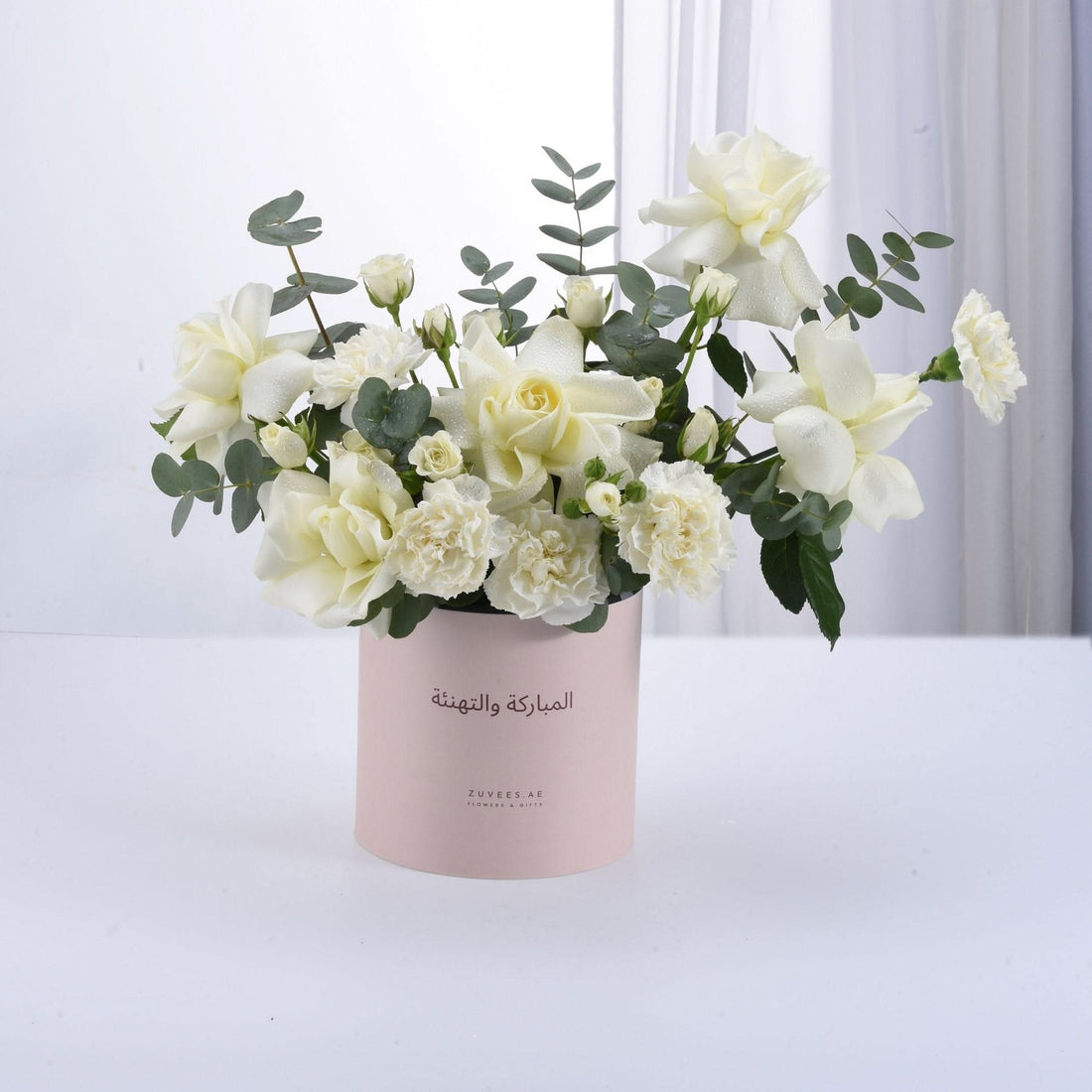 Soft white roses and carnations in pink box with Arabic greeting.