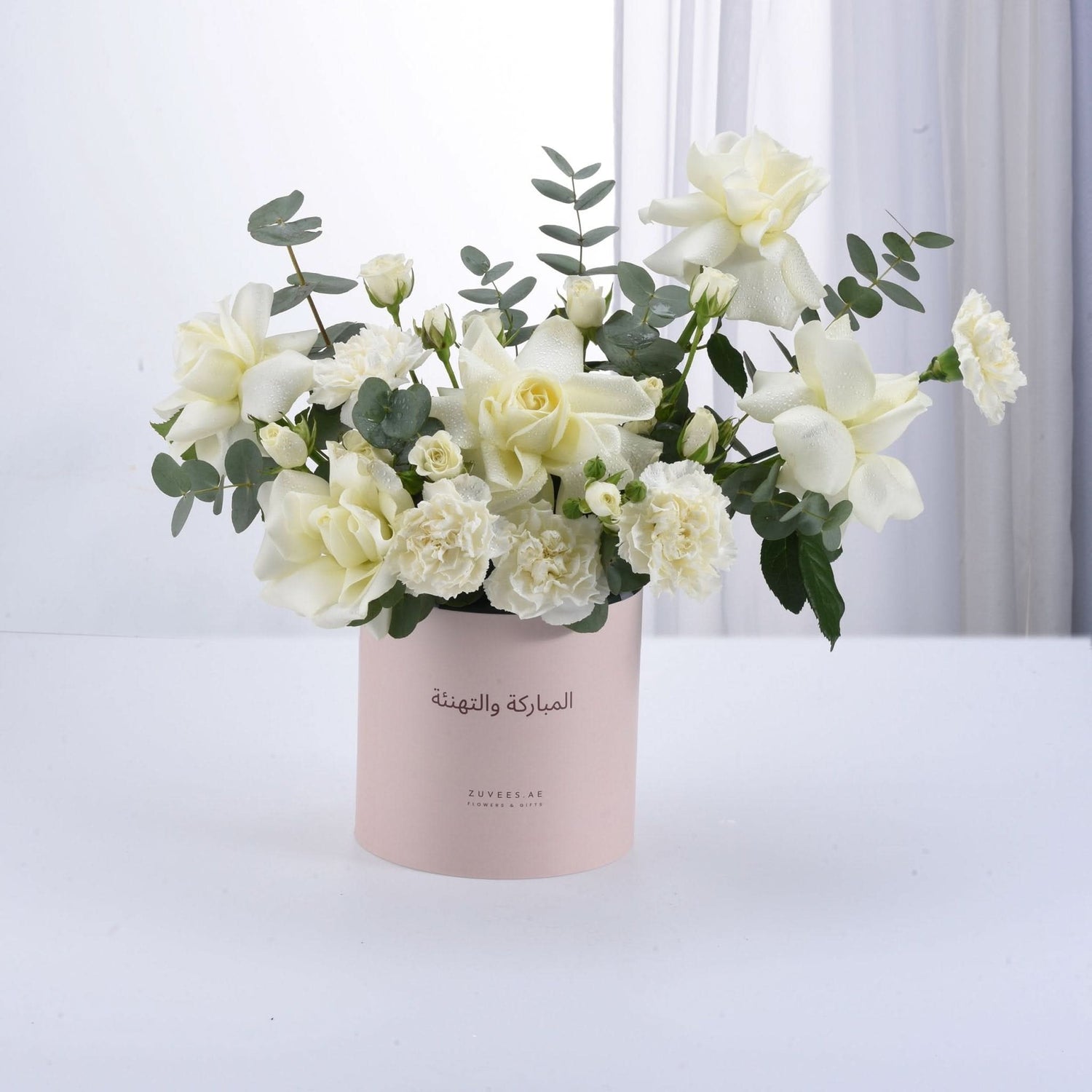 Soft white roses and carnations in pink box with Arabic greeting.