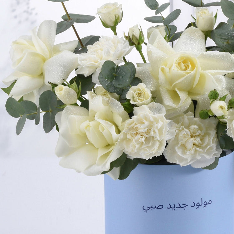 White roses and carnations glisten with dewdrops in a light blue vase.