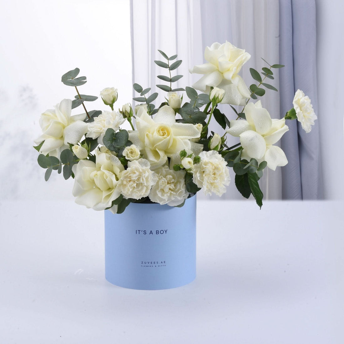 Light blue box holds dew-kissed white roses and eucalyptus, celebrating "It&