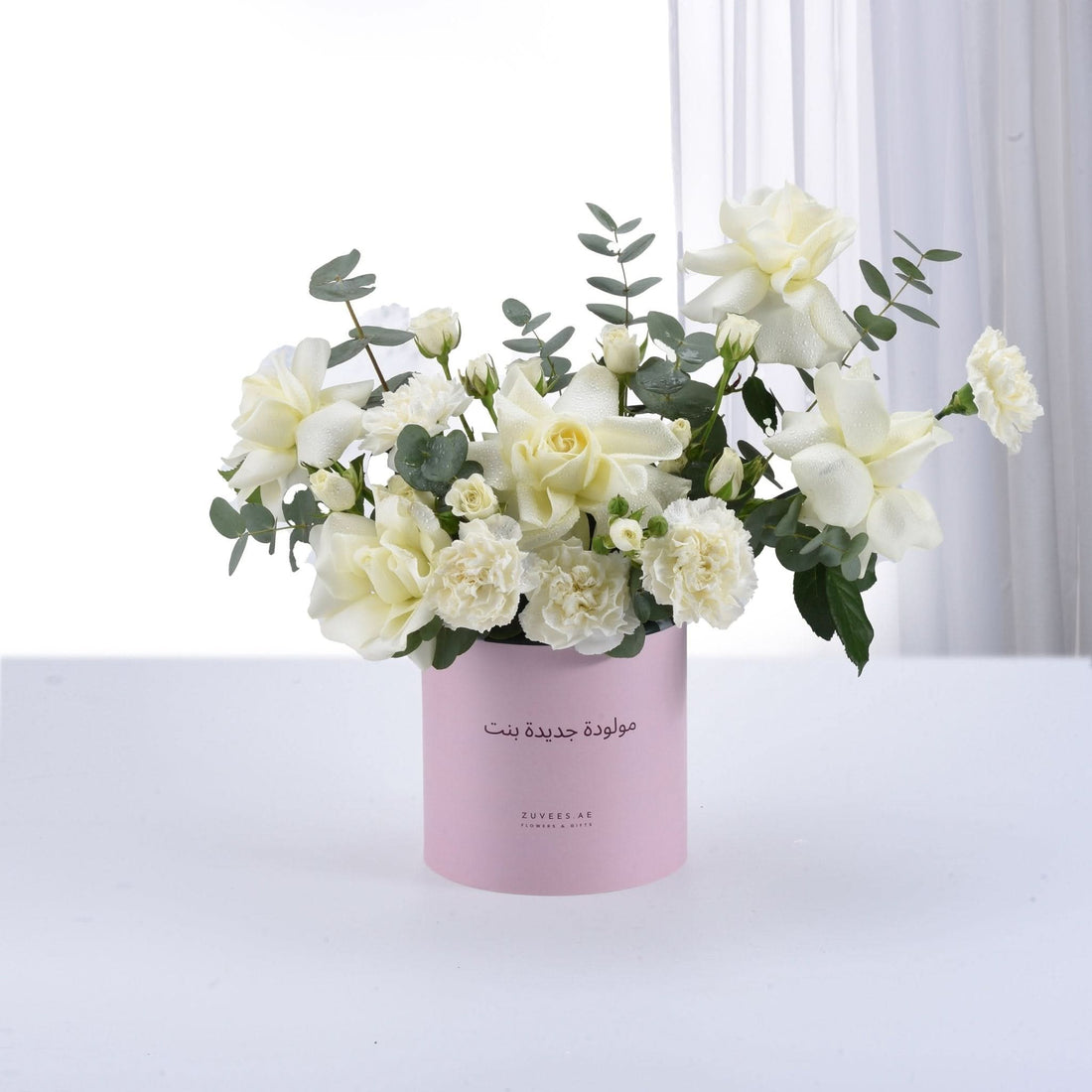 Elegant white rose and carnation bouquet in pink cylinder, adorned with eucalyptus, dewdrops, and Arabic "Happy Birthday Girl" text.