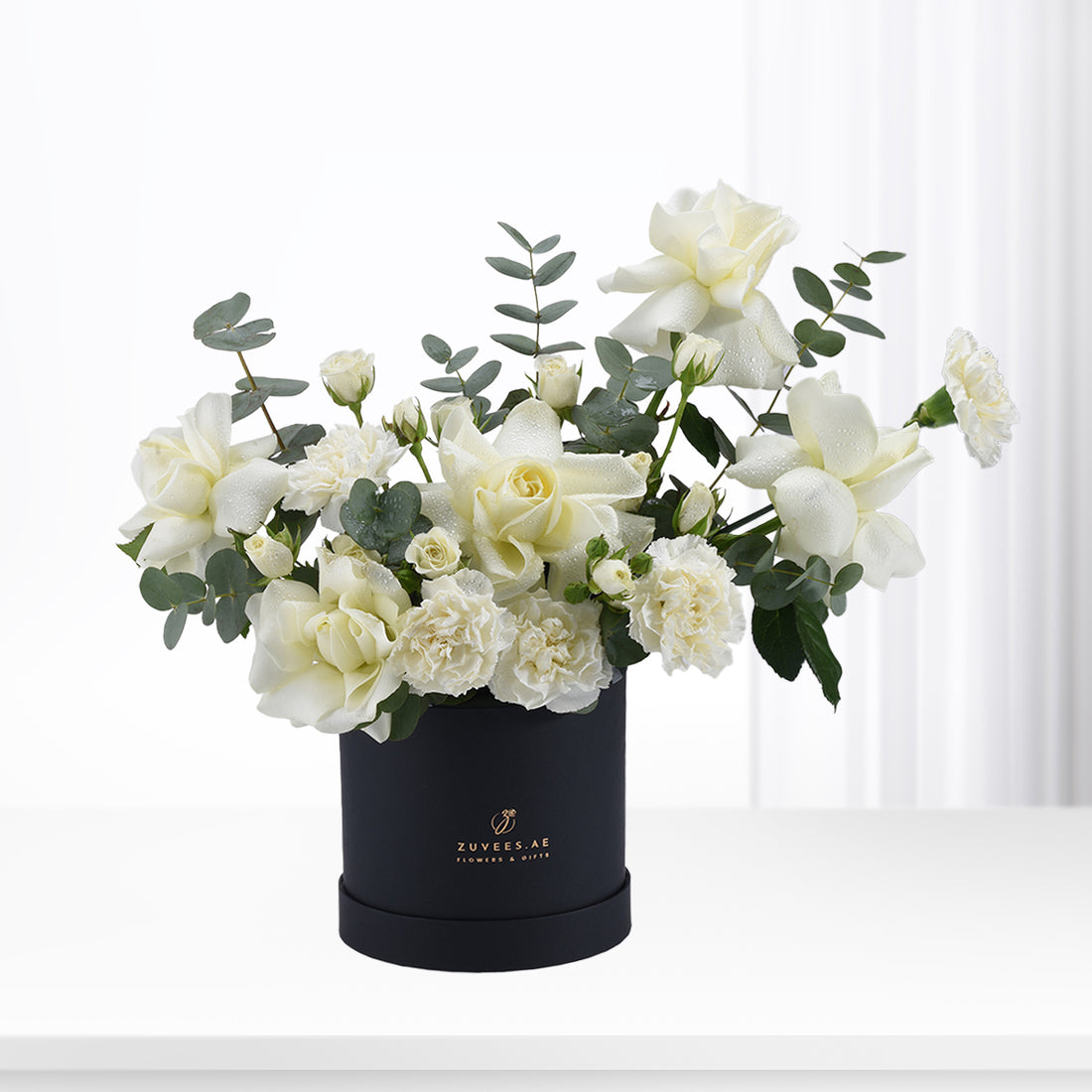 Elegant white roses and eucalyptus in matte black cylindrical gift box.
