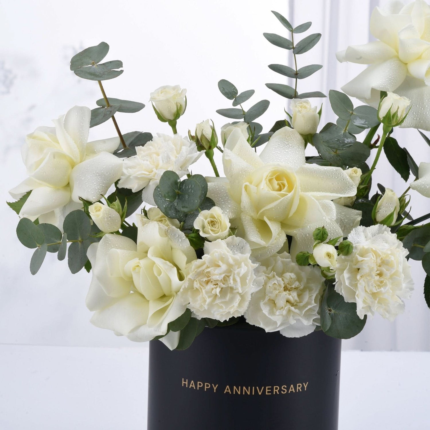 Elegant white roses and carnations with dewdrops in black "Happy Anniversary" vase.