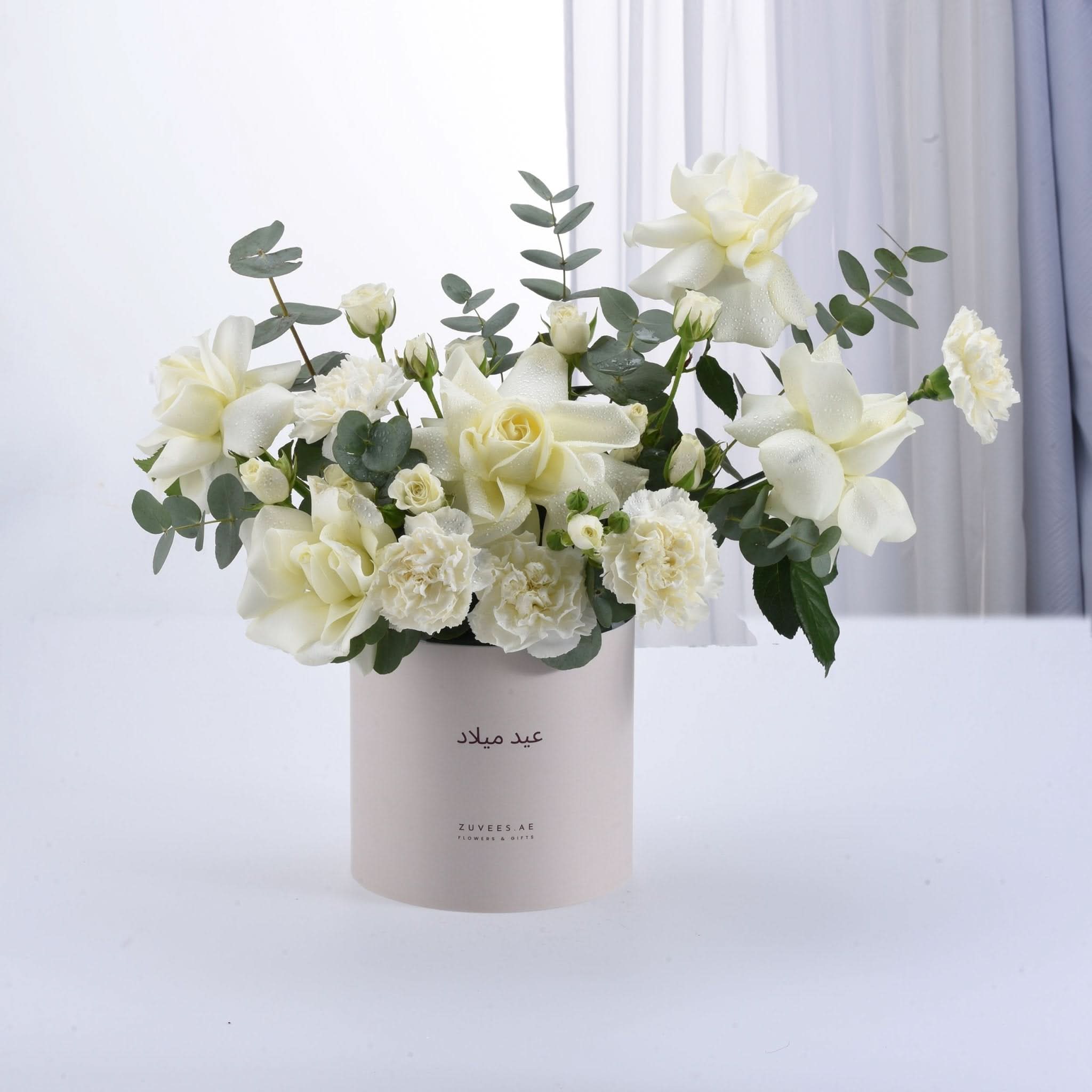 Elegant white roses and eucalyptus in minimalist beige cylinder vase.