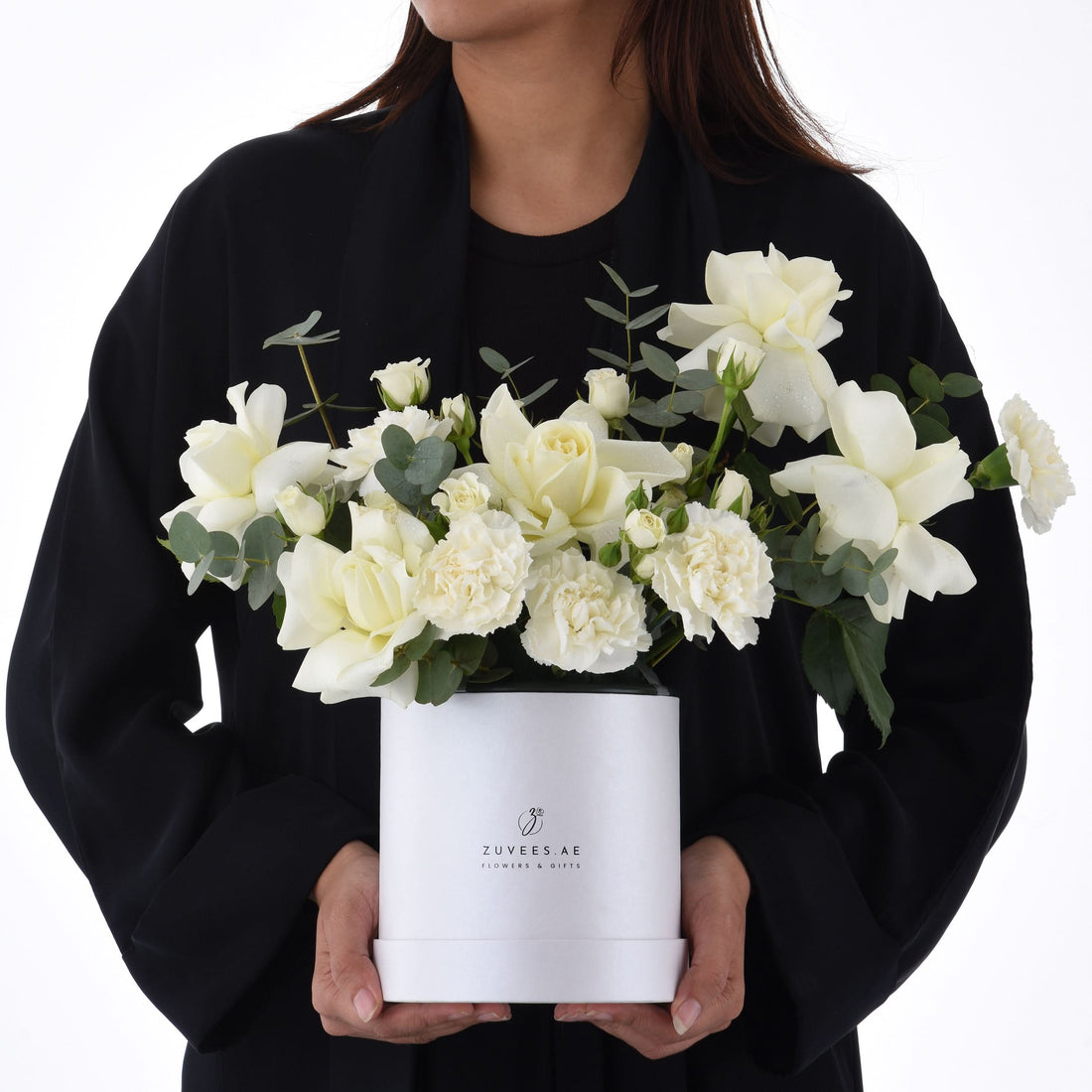 Elegant white roses and carnations in sleek white box held by person.