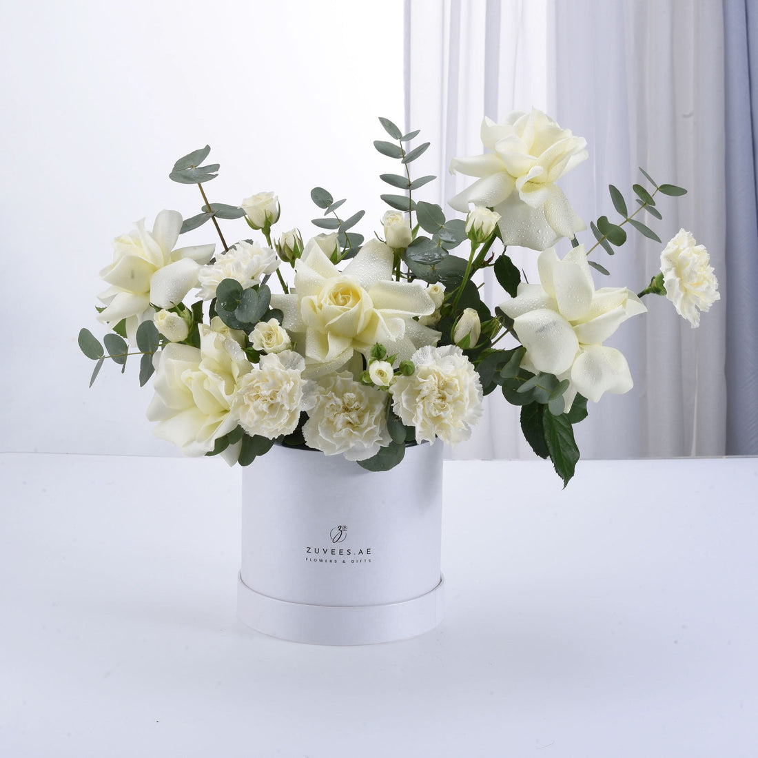 Elegant white roses and carnations in sleek white cylindrical gift box.