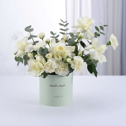 Elegant white rose and carnation bouquet in mint green cylindrical vase.