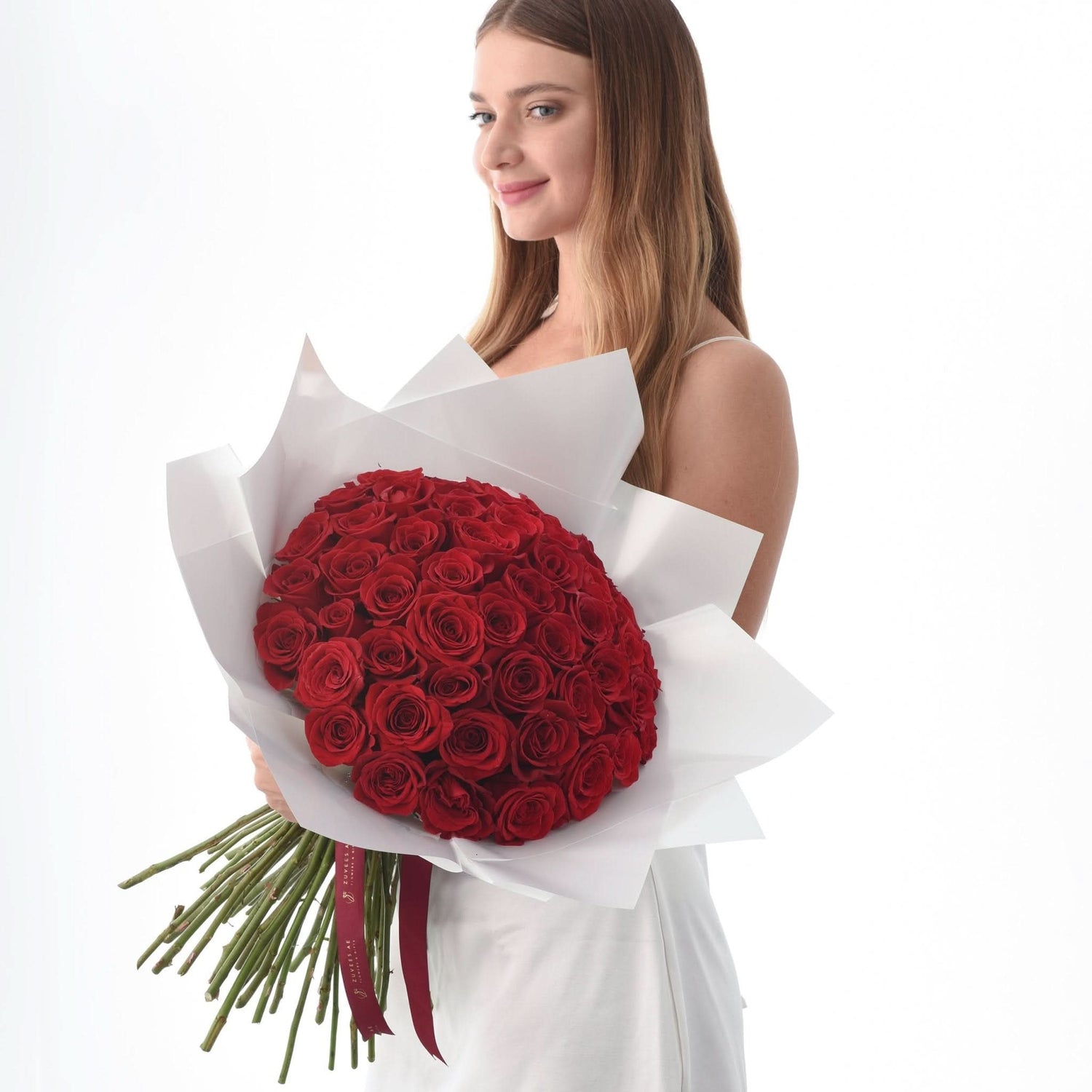 Woman holds lush red rose bouquet wrapped in white paper against bright white background.