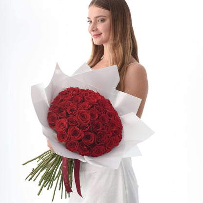Woman holds lush red rose bouquet wrapped in white paper against bright white background.