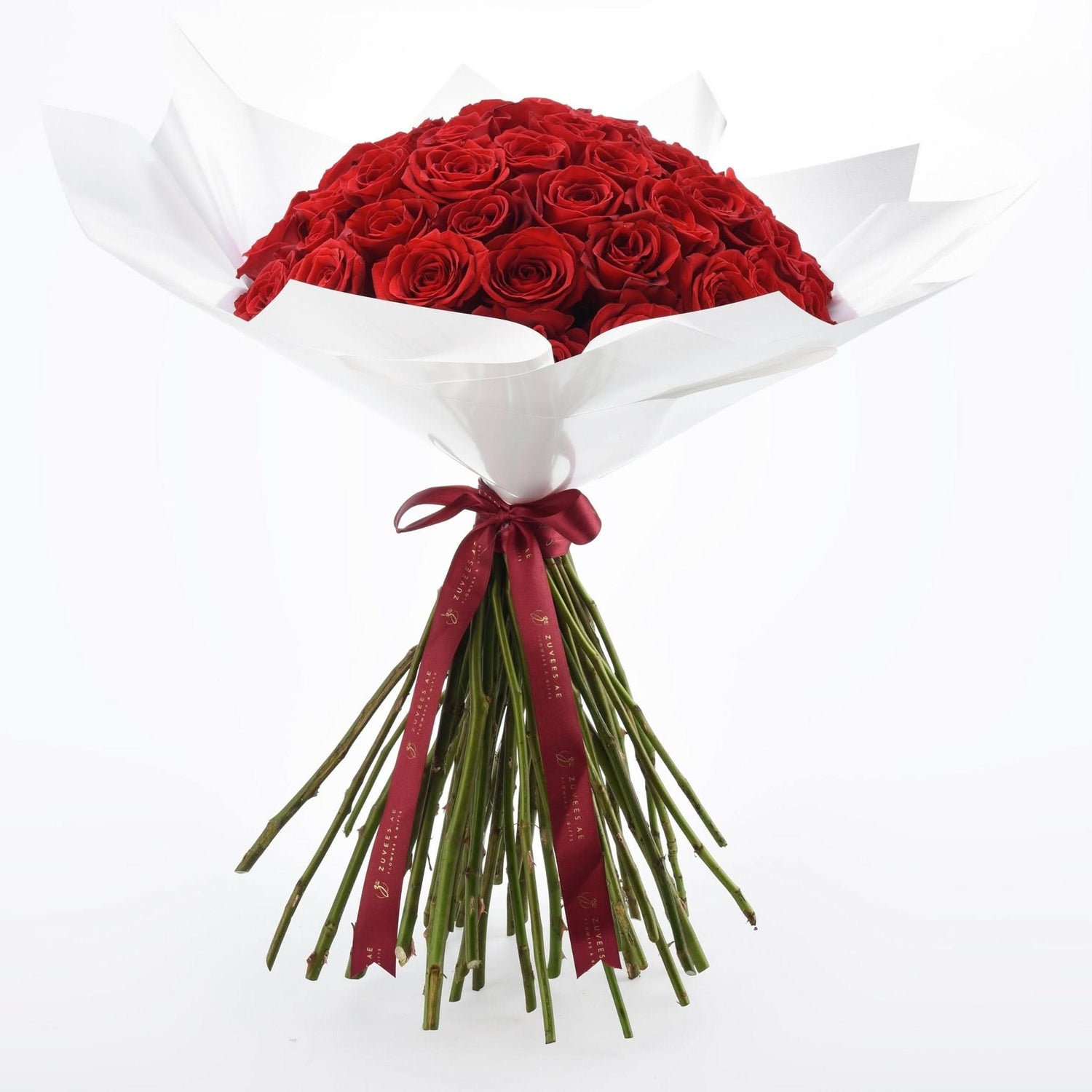 Vibrant red roses in crisp white paper, tied with burgundy ribbon.