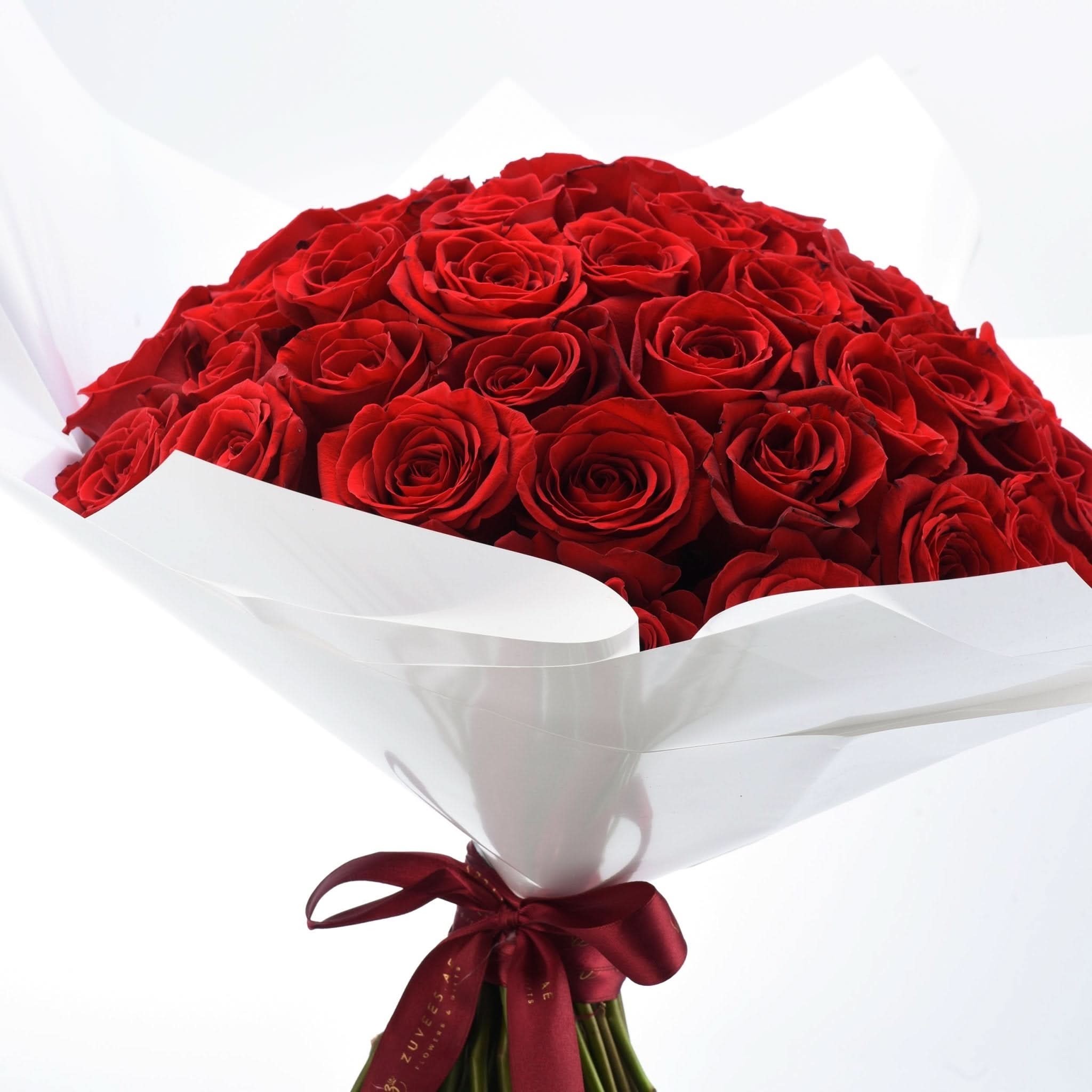 Vibrant red roses in white wrap, tied with burgundy ribbon, elegant and romantic.