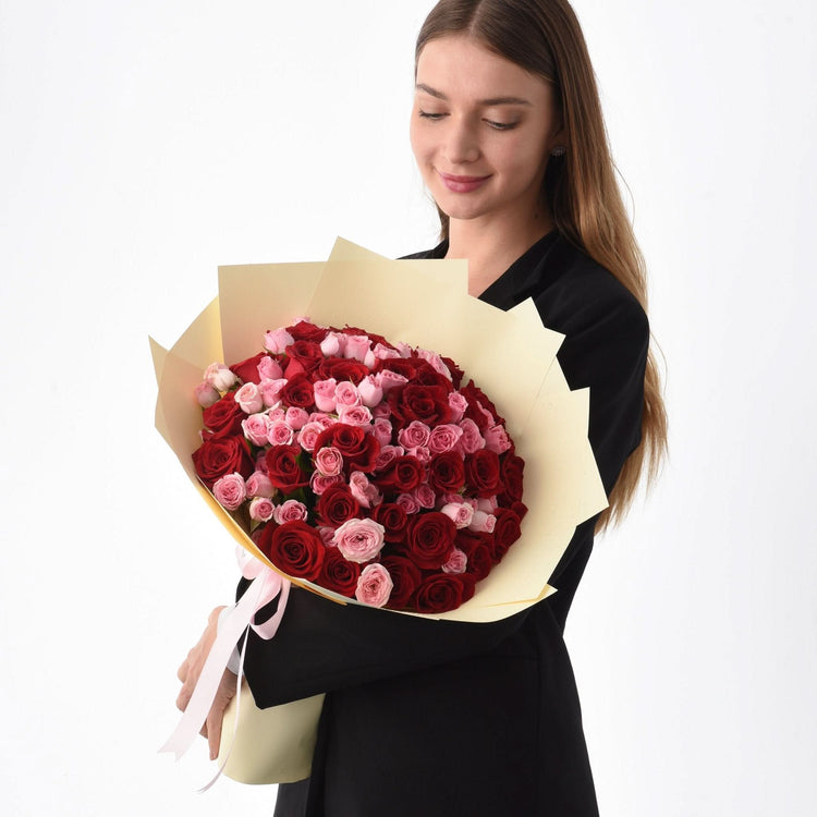 Woman holds vibrant red and pink rose bouquet wrapped in cream paper.