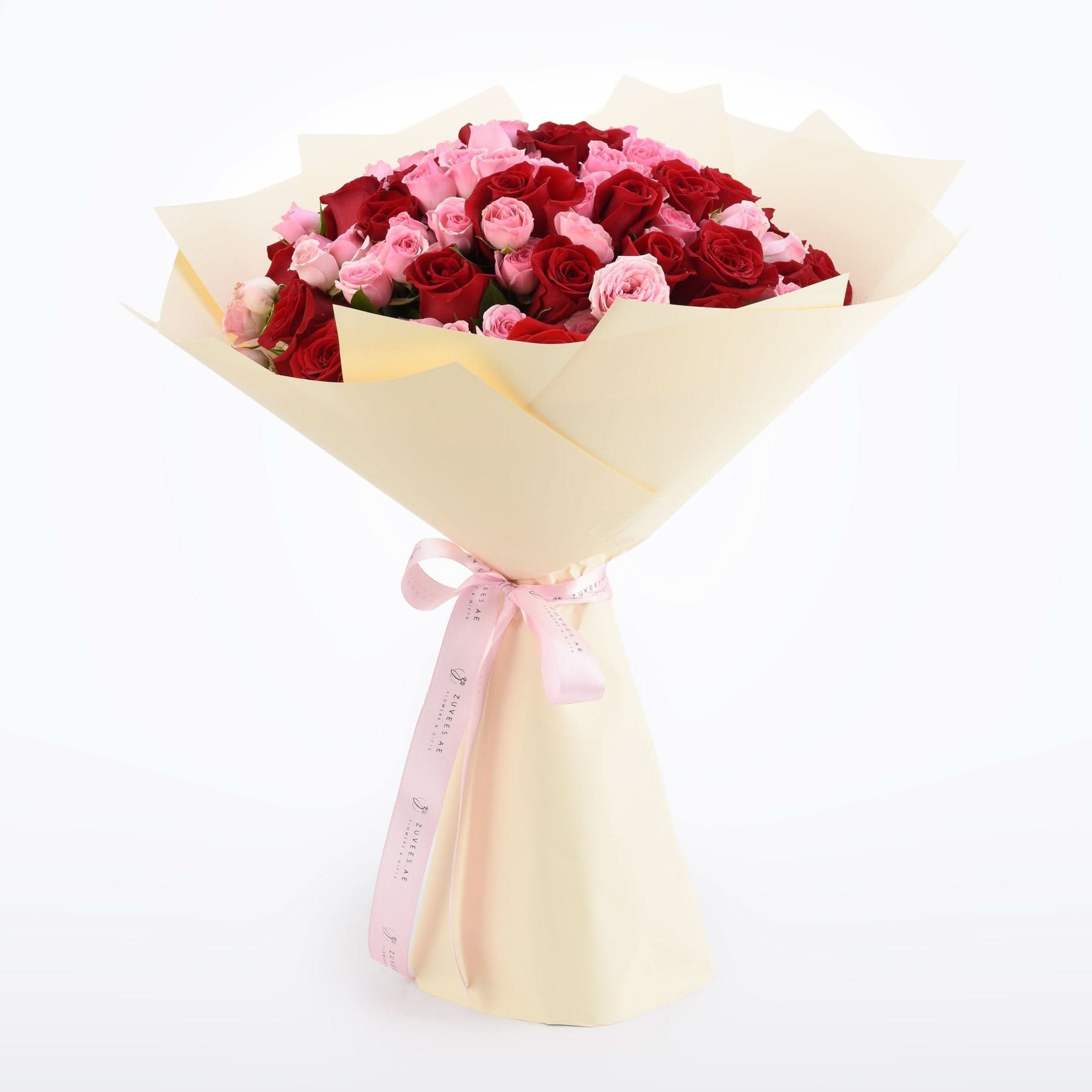 Vibrant red and pink roses wrapped in cream paper with pink ribbon bow.