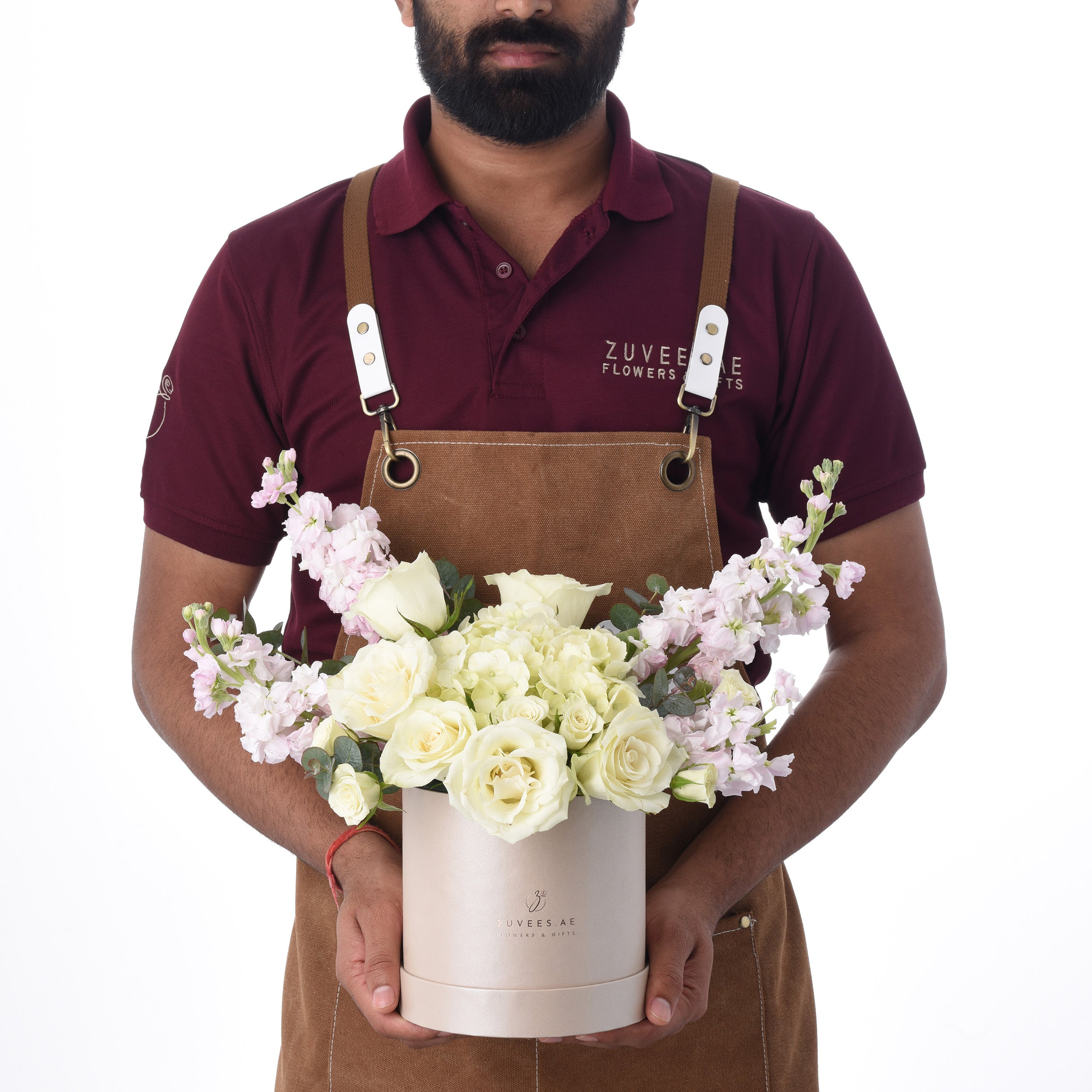 Florist presents elegant white rose and pink bloom arrangement in branded rose-gold box.
