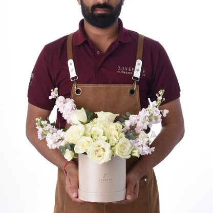 Florist presents elegant white rose and pink bloom arrangement in branded rose-gold box.