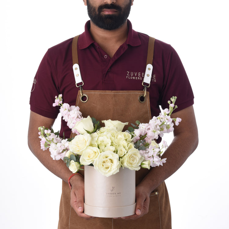 Florist presents elegant white rose and pink bloom arrangement in branded rose-gold box.
